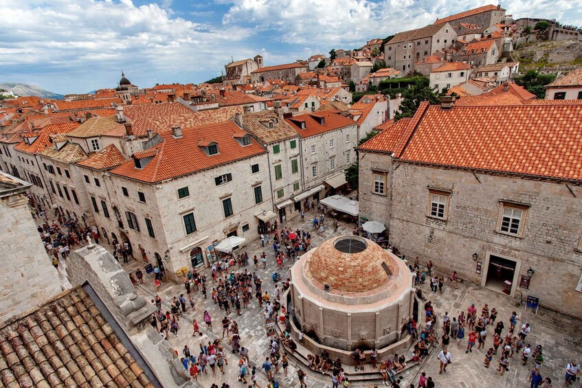 A historic town square with a central fountain, surrounded by buildings with red-tiled roofs. 3