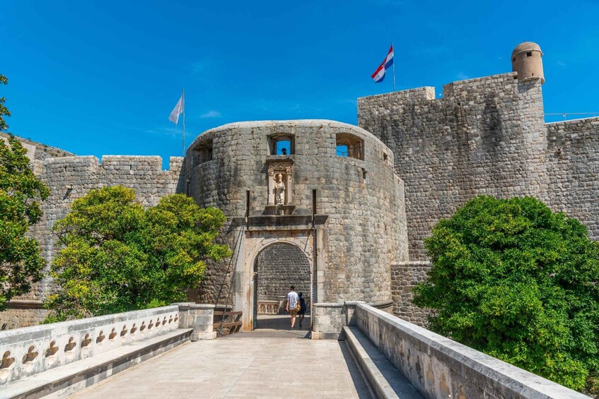 A historic stone castle with a central round tower, flags, and a paved entrance pathway. 5
