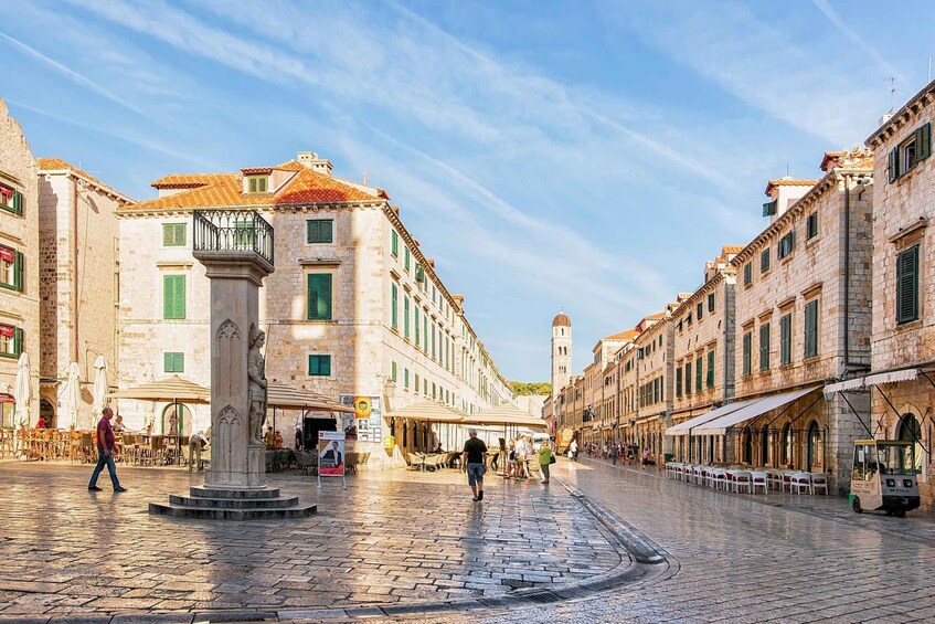 A cobblestone square with historic buildings, a statue, and outdoor seating. 1