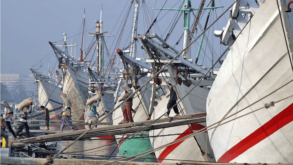 A harbor with multiple sailing ships docked, workers on the deck, and a clear sky. 2