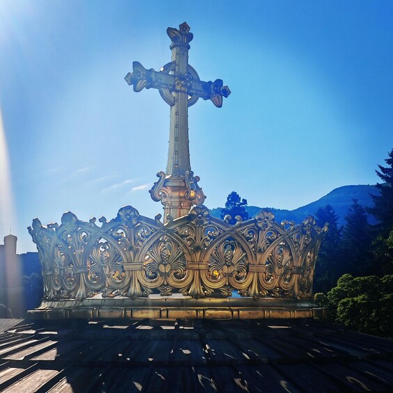 A large ornate cross monument with intricate designs, set against a clear blue sky and surrounded by greenery. 2