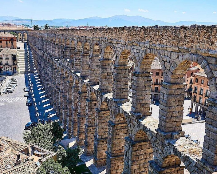 An ancient stone aqueduct with arches, a street with cars, and buildings in the background. 3