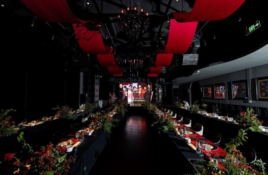 A dimly lit restaurant with red drapes and a long table set for a meal. 2