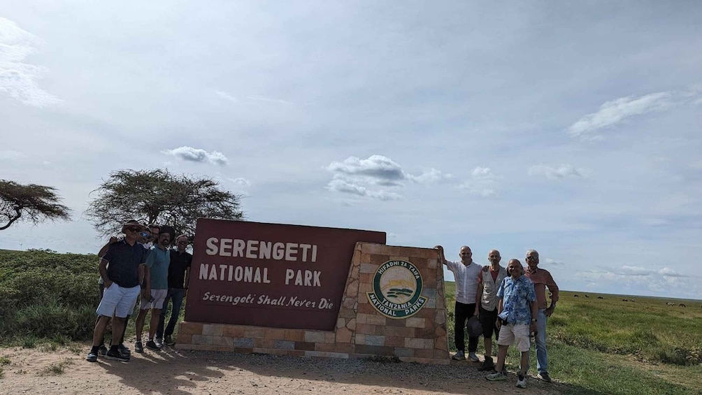 A group of people standing in front of a sign for Serengeti National Park. 4