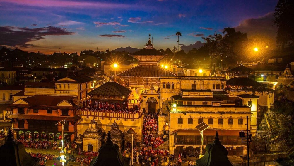 A historic temple complex at dusk with illuminated structures and a crowd of people. 2