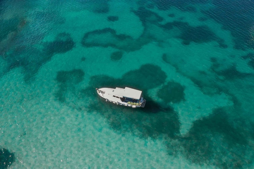 An aerial view of a boat anchored in clear turquoise waters with visible coral formations. 1