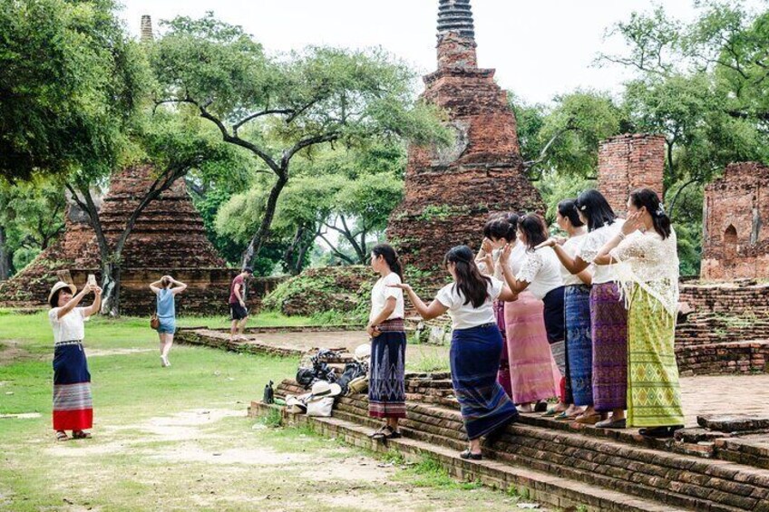 A group of people in traditional attire standing on temple steps, with ancient brick structures and trees in the background. 5