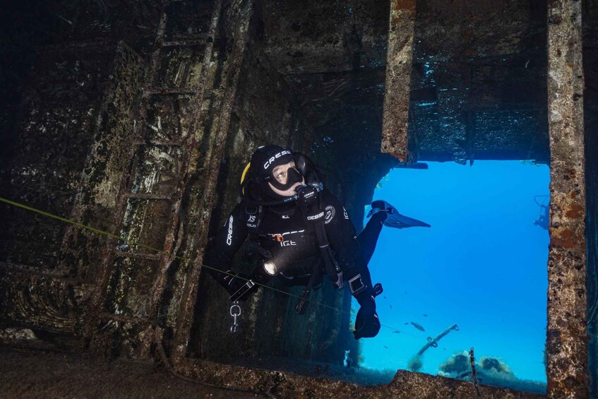 A diver in black scuba gear with a mask and fins, exploring an underwater cave with visible rock formations and water. 2