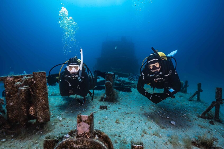 Two scuba divers exploring an underwater site with visible structures and debris. 3