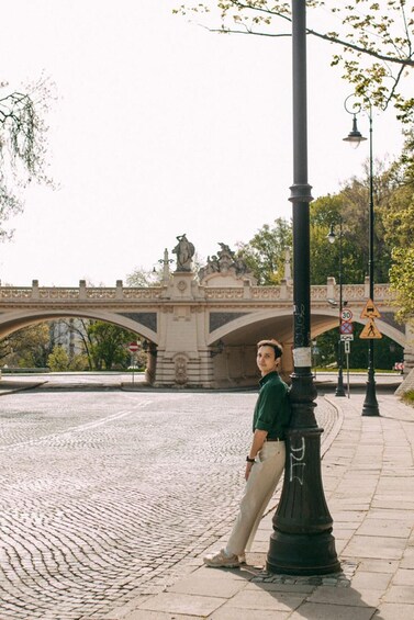 A man standing on a cobblestone path with a bridge and statues in the background. 3