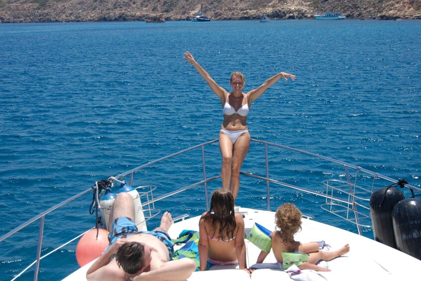 A woman in a bikini standing on a boat with her arms raised, surrounded by people relaxing on the deck. 2