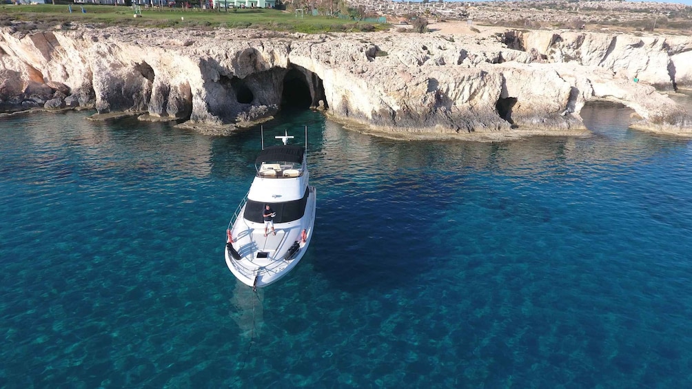 A boat anchored near a rocky coastline with clear blue water. 1
