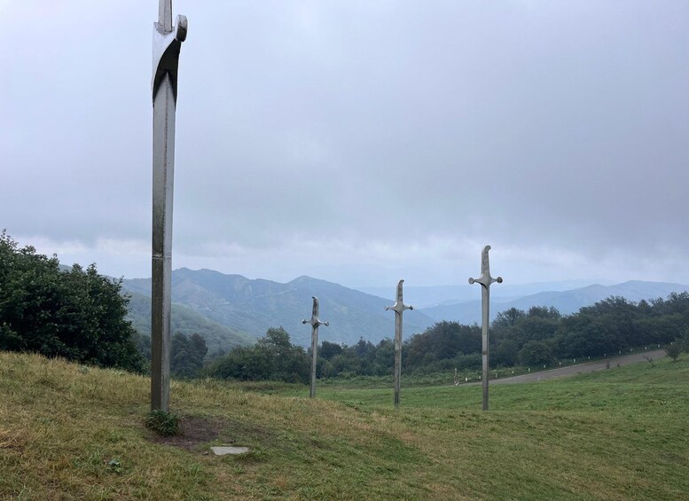 A grassy field with three wooden crosses and a mountain range in the background. 1