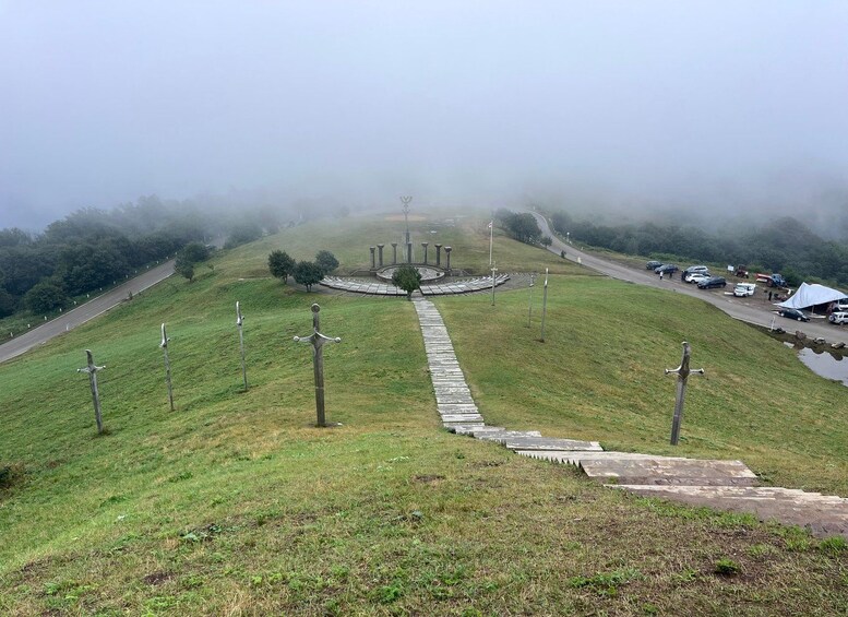 A foggy landscape with a circular monument, a road, and parked cars. 4