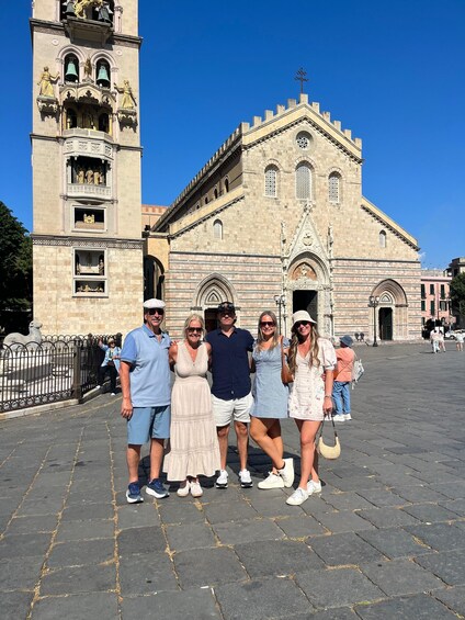 A group of people standing in front of a historic church with a bell tower. 3