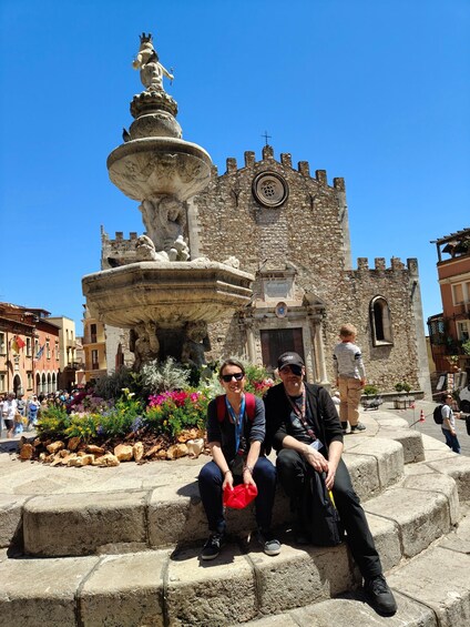 A historic stone building with a clock tower and a fountain with statues. 5