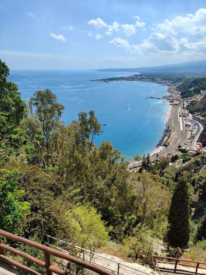 A coastal landscape with a winding road, dense greenery, and a clear blue sea. 3