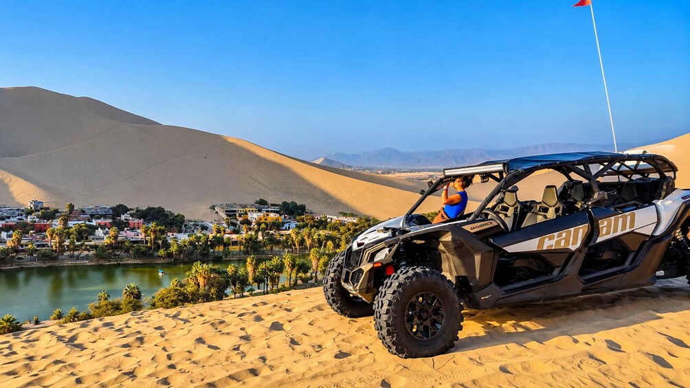 A dune buggy parked on sand dunes with a desert landscape and a body of water in the background. 2
