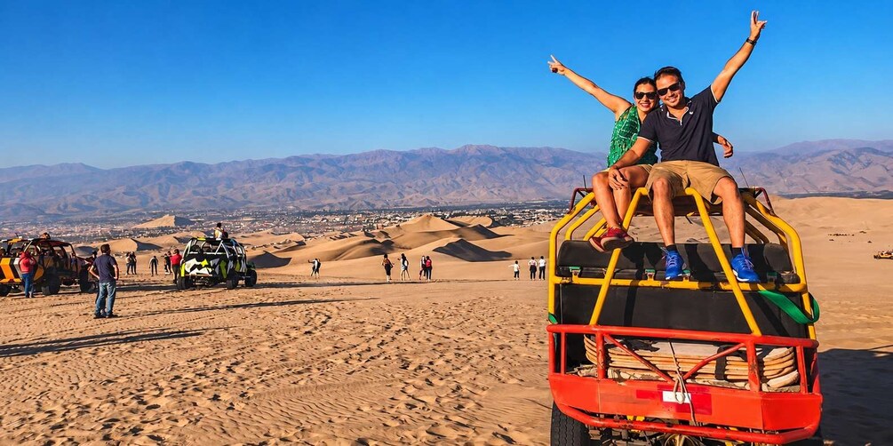 A desert landscape with sand dunes and a group of people on a dune buggy. 4
