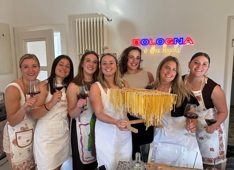 A group of people in a kitchen, holding wine glasses and a pasta strainer. 2