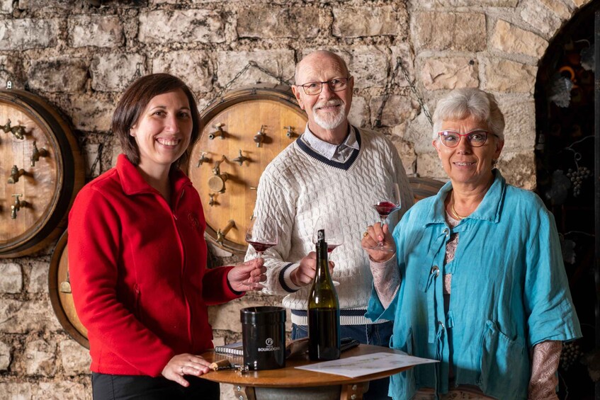 Three people in a cellar with wine barrels and a bottle of wine. 4