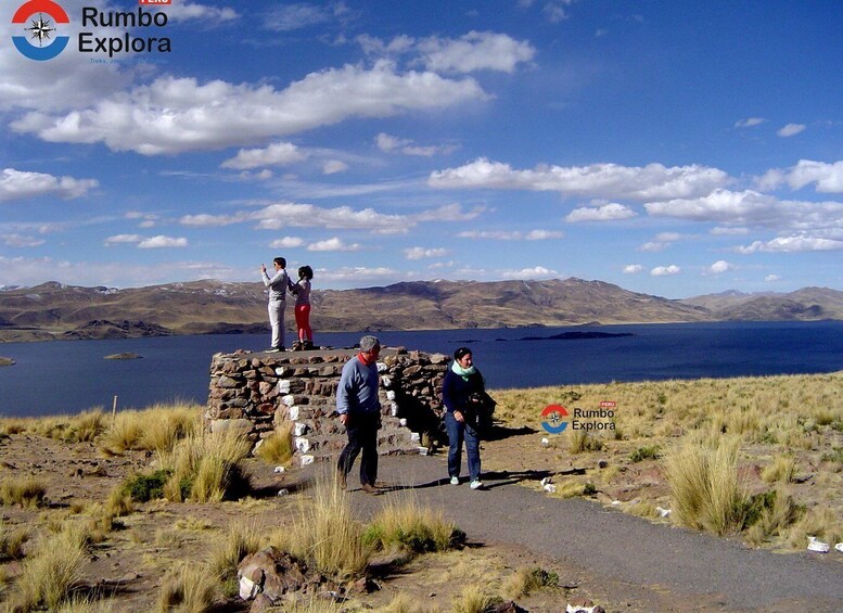 A group of people standing on a stone structure overlooking a lake with mountains in the background. 3