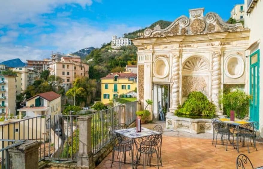 A terrace with outdoor furniture, a decorative archway, and buildings in the background. 3