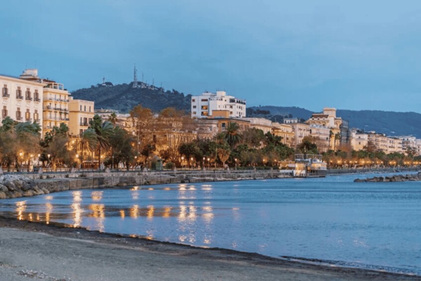 A coastal cityscape with buildings, a body of water, and a hill in the background. 2