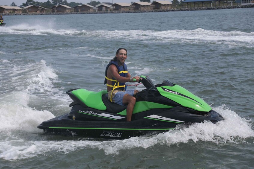 A person riding a green and black Kawasaki jet ski on a body of water. 1