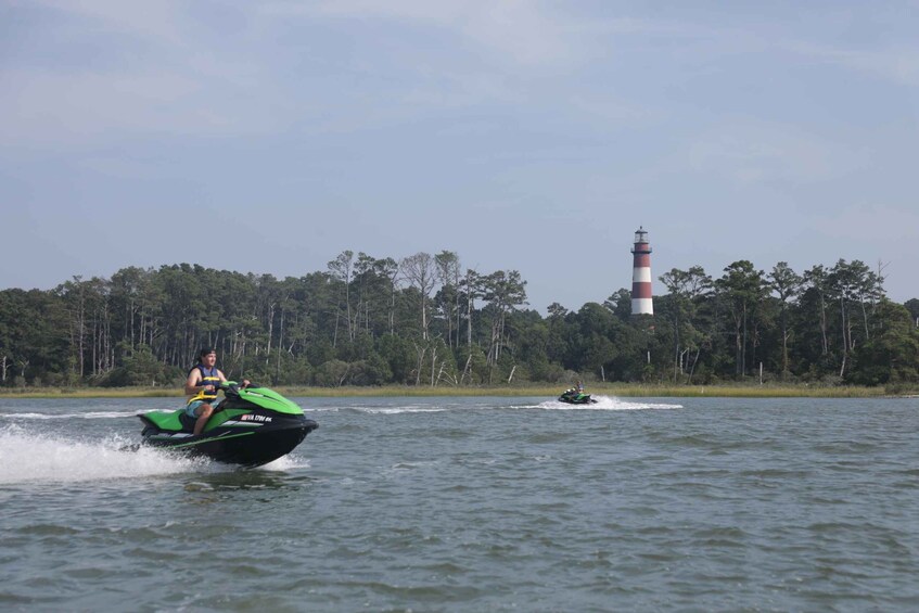 A person riding a green jet ski on water with a lighthouse in the background. 5