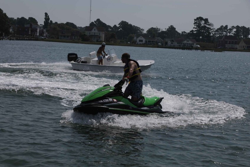 A person jet skiing on a green jet ski on the water with a house-lined shore in the background. 2