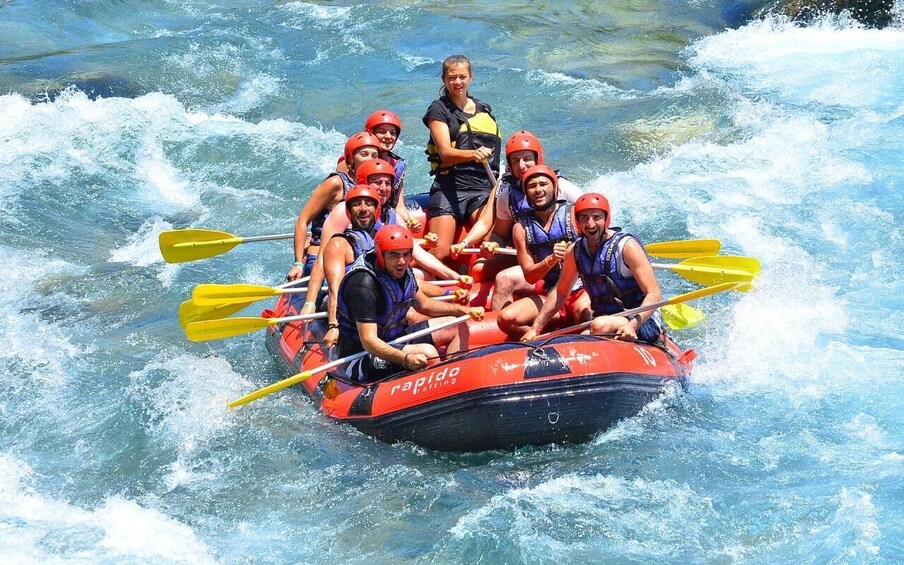 A group of people in a red and black inflatable raft navigating through white water rapids. 4