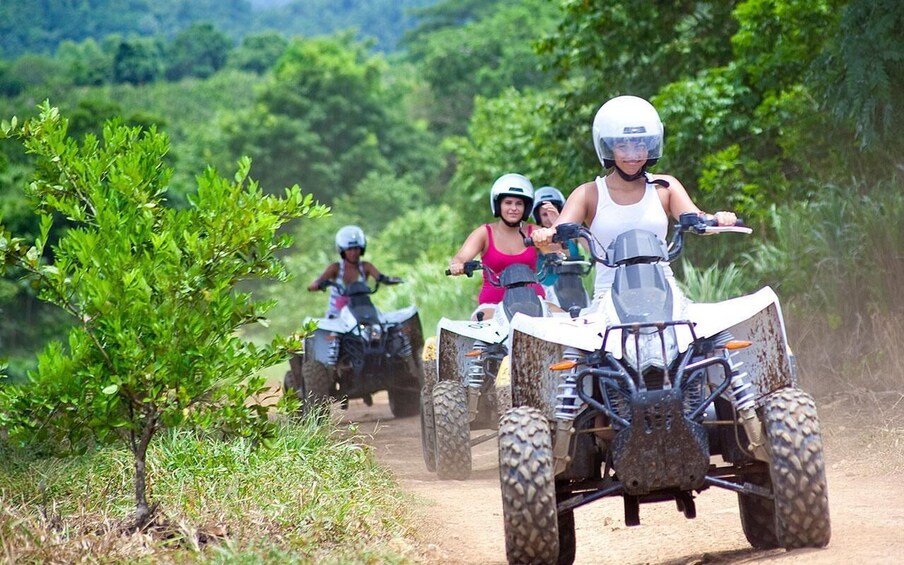 Four people riding atv's on a dirt path surrounded by greenery. 5