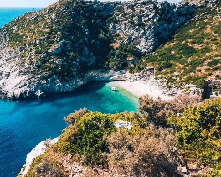 A coastal landscape with rocky cliffs, a sandy beach, and clear turquoise waters. 4