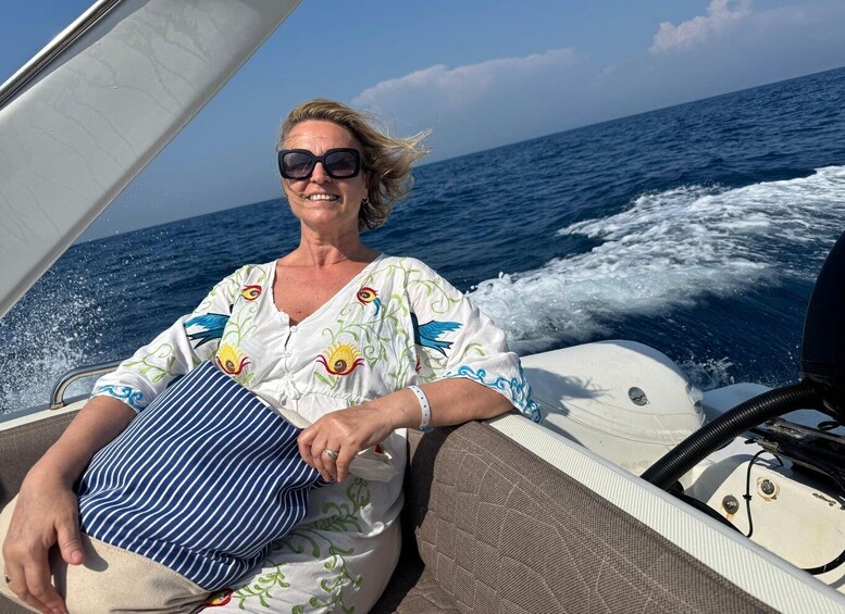 A person on a boat with a white and blue patterned shirt, holding a striped pillow, with the ocean and waves in the background. 3