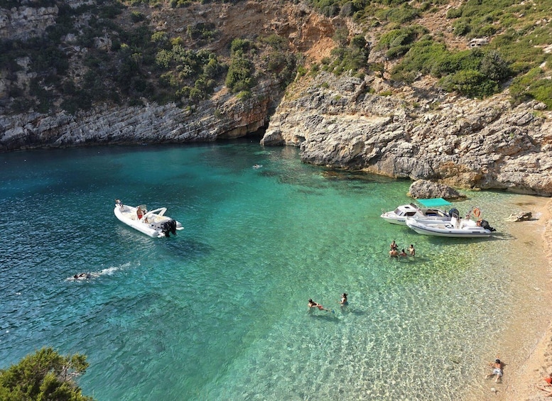 A clear turquoise sea with boats, rocky cliffs, and people enjoying the beach. 2