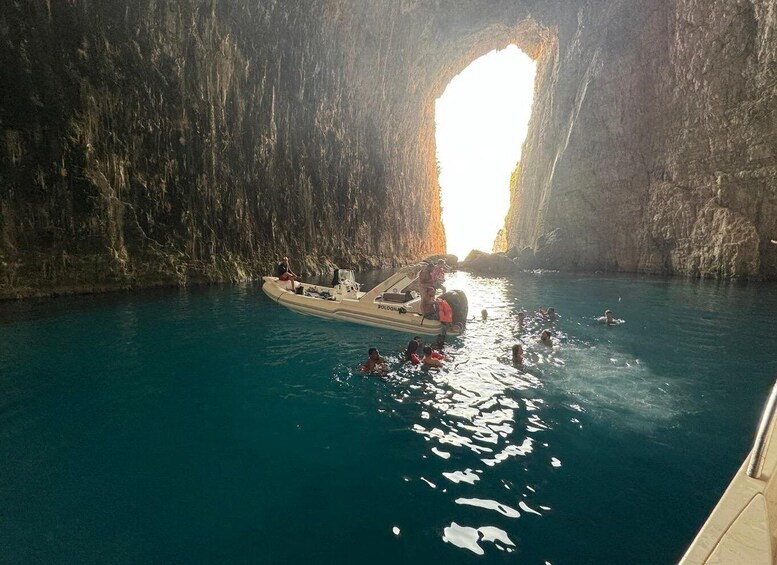A boat in a clear blue water body with a rocky cave entrance in the background. 5