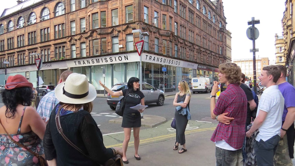 A group of people standing on a street in front of a building with 'TRANSMISSION' signage. 4