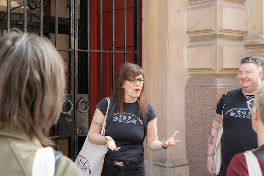 A woman in a black t-shirt with a band logo, gesturing while talking to a group of people. 3