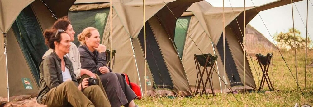 A group of people sitting outside a large tent in a grassy field. 2