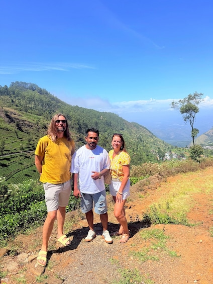 Three people standing on a dirt path with a mountainous landscape in the background. 4