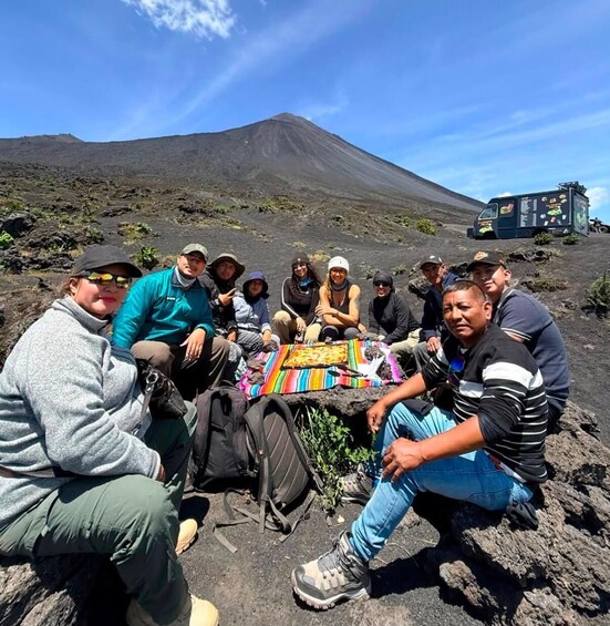 A group of people sitting on a blanket in a volcanic landscape with a mountain in the background. 3