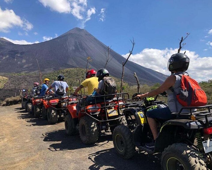 A group of people on ATVs on a dirt path with a volcano in the background. 1