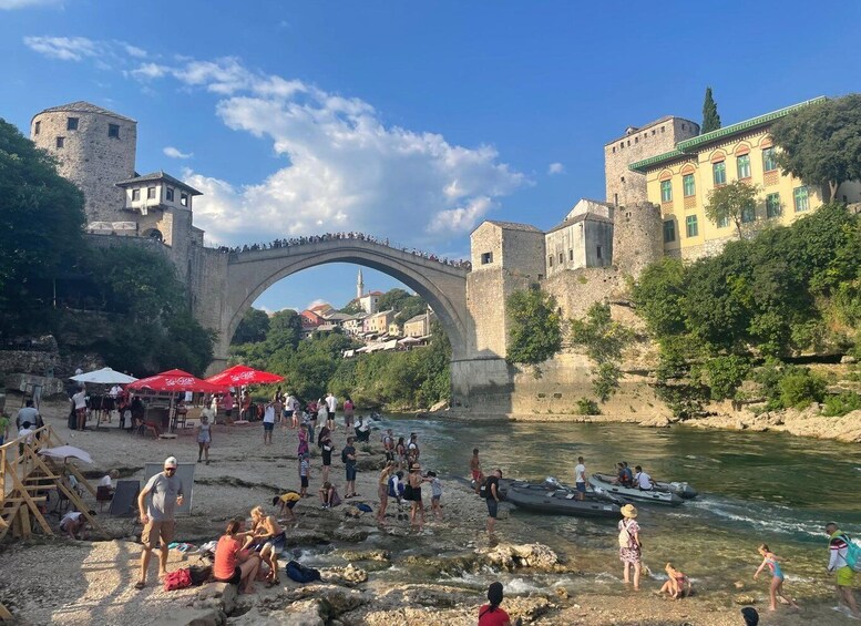A stone bridge over a river, people relaxing by the water, and historic buildings in the background. 4