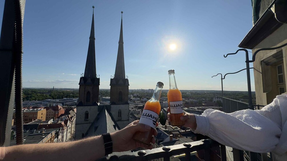 Two people holding bottles of Lujah juice on a balcony overlooking a city with tall spires. 5