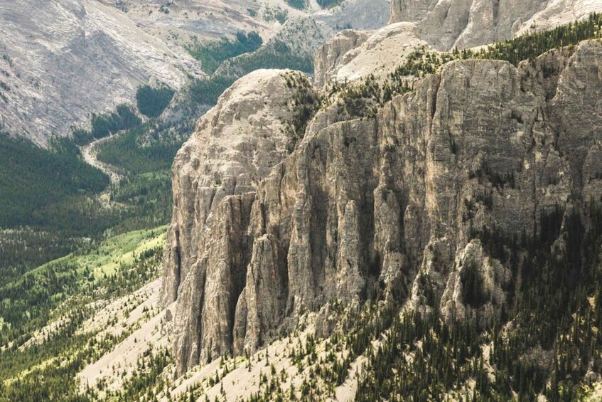 A rugged mountain landscape with prominent vertical rock formations and a valley with scattered trees. 2