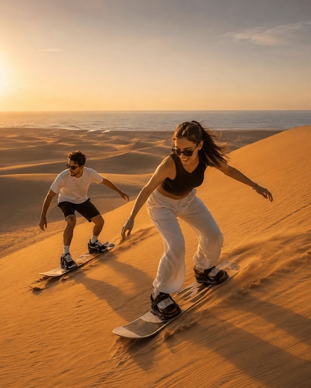 Two people snowboarding down a sand dune with a sunset in the background. 5