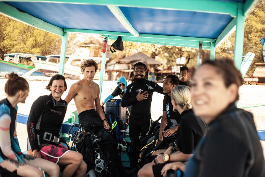 Un grupo de personas con trajes de neopreno y equipo de buceo, reunidas bajo una zona cubierta con techo azul, probablemente preparándose para una actividad de buceo. 2