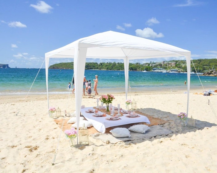 A beach with a white canopy, a table set for a meal, and a clear blue sea in the background. 2
