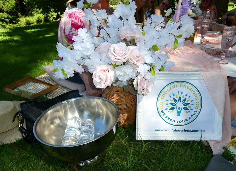 A picnic setup with a metal bowl, a basket with flowers, and a sign with a logo and website. 5